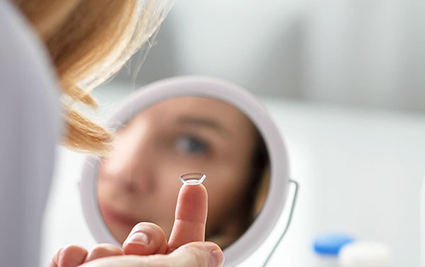 lady looking into handheld mirrow with a contact on her fingers